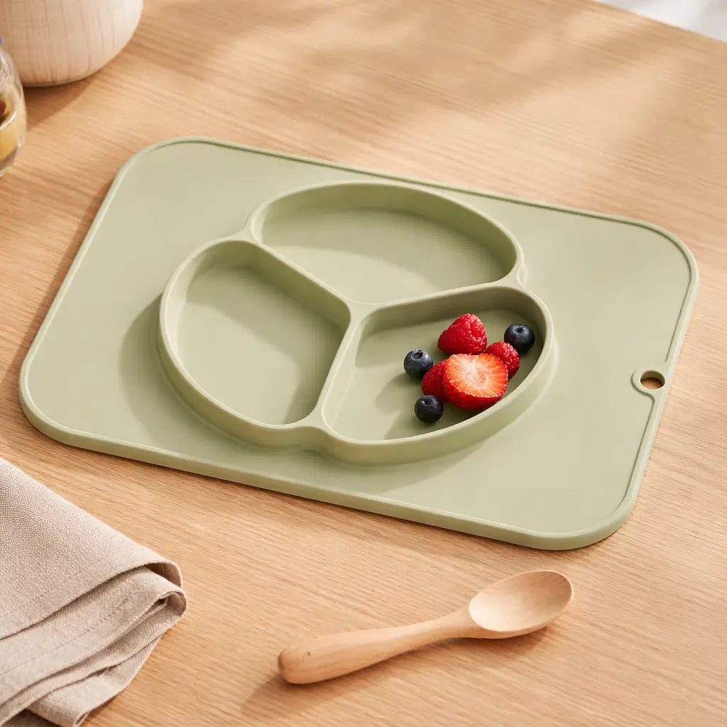 Baby silicone non-slip plate with placemat featuring compartments for fruits on a wooden table.