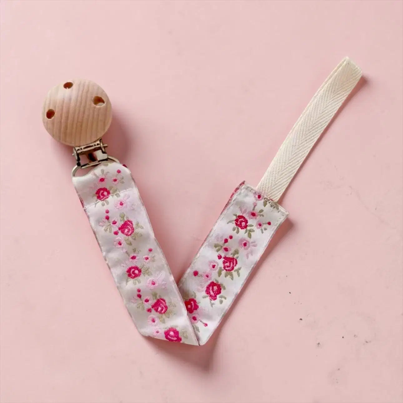 Giggle Bubs Luxe Dummy Clip for babies in floral design with natural wooden clip on pink background.