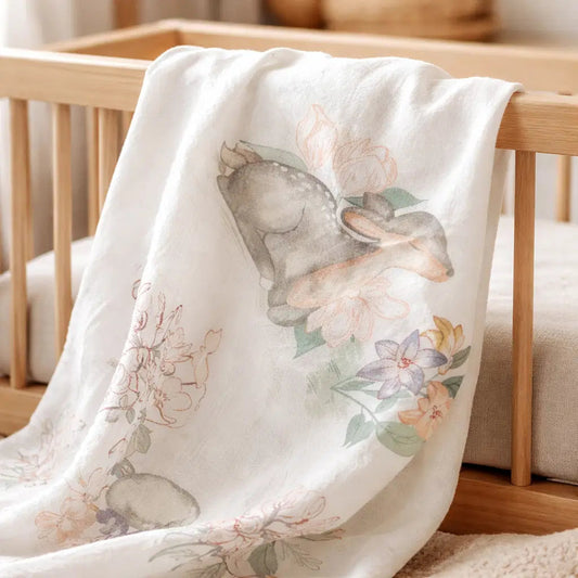 Bubs Universe organic cotton muslin wrap featuring a whimsical fawn and floral print draped over a wooden baby cot.